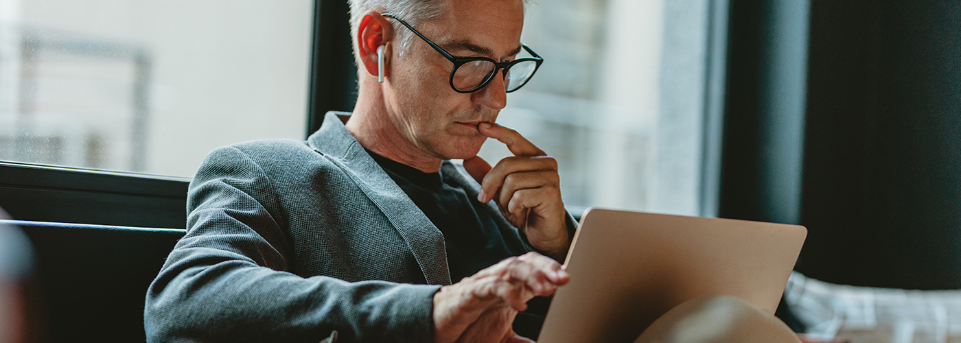 Businessman looking at laptop and thinking. Businessman reading emails on laptop in office lobby.